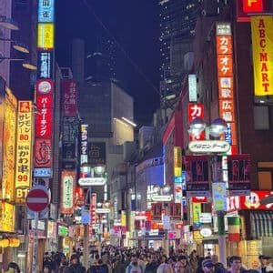 Un viaggio di gruppo WeRoad percorre una vivace strada cittadina di notte, illuminata da alti edifici e colorate insegne al neon giapponesi.