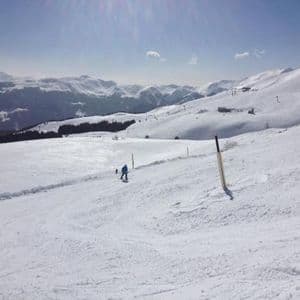 Una persona con una giacca blu scia su un'ampia pista innevata con montagne sullo sfondo sotto un cielo soleggiato.