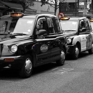 Una fila de taxis negros de Londres estacionados en una calle de la ciudad, capturados en blanco y negro con solo sus letreros de taxi naranjas a color.