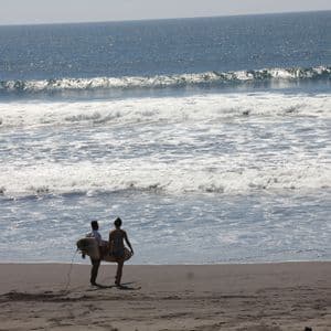 Un uomo e una donna trasportano tavole da surf camminando su una spiaggia sabbiosa verso le onde dell'oceano.