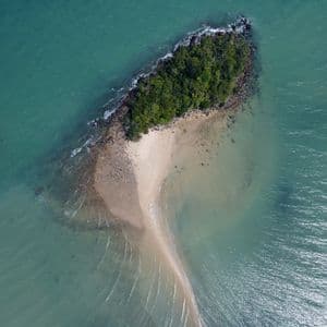 Veduta aerea di una piccola isola alberata con una lingua di sabbia che si estende nelle calme acque turchesi.