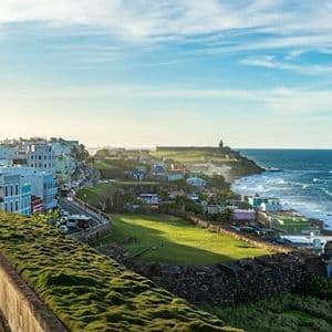 Una vista dall'alto di una colorata città costiera e una fortezza sul mare, con un muro di pietra muschioso in primo piano.