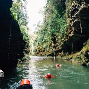 Un viaggio di gruppo WeRoad, con caschi e giubbotti di salvataggio, scende lungo un fiume attraverso uno stretto e lussureggiante canyon verde.