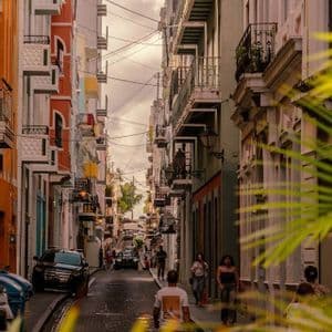 Una veduta su una stretta strada acciottolata, con persone che passeggiano tra colorati edifici a più piani dotati di balconi.