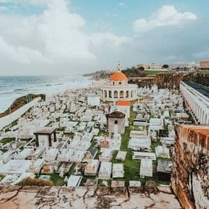 Veduta dall'alto di un cimitero costiero con lapidi bianche e una cappella dalla cupola arancione, affacciato sull'oceano.