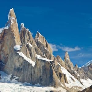 Zerklüftete Granit-Bergspitzen mit Schneefeldern und einem Gletscher am Fuße unter klarem blauem Himmel.