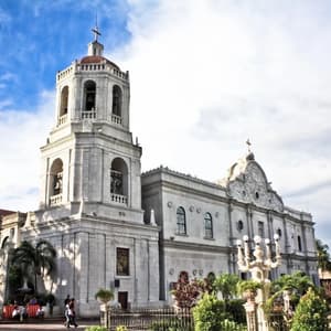Una grande cattedrale in pietra bianca con un campanile ornato si erge sotto un cielo blu con nuvole bianche.