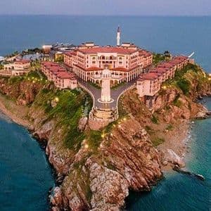 Vue aérienne d'un grand complexe hôtelier illuminé sur une péninsule rocheuse entourée par la mer au crépuscule.