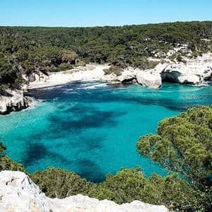 Une crique isolée aux eaux turquoises, une plage de sable blanc et des falaises couvertes d'une dense forêt verdoyante.