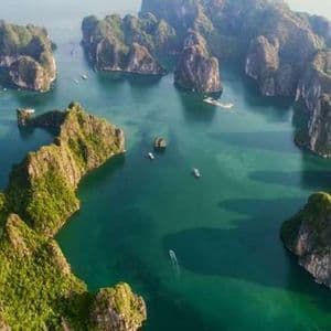 Vista aerea di numerose isole calcaree dalle cime verdi che si ergono da acque calme e turchesi, con piccole barche che navigano tra di esse.
