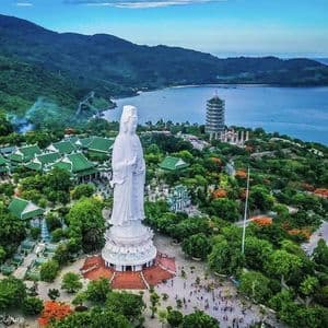 Una gigantesca statua bianca di una divinità femminile si erge in un complesso templare con una pagoda, che domina una baia boscosa.