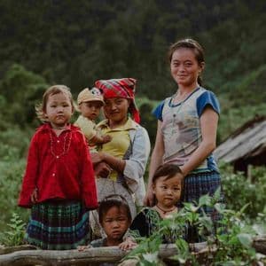 Un gruppo di donne e bambini in abiti colorati posano insieme per una foto in un paesaggio rurale lussureggiante e verde.