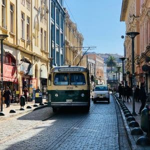 Un filobus vintage verde e crema percorre una strada acciottolata tra edifici colorati in una giornata di sole.