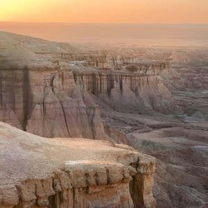 Eine weite Canyon-Landschaft mit geschichteten Felsformationen, die sich unter einem warmen, leuchtenden Himmel bei Sonnenaufgang in die Ferne erstrecken.