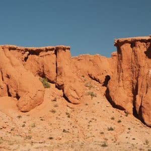 Erodierte rote Felsformationen stehen in einer Wüstenlandschaft unter einem klaren blauen Himmel.