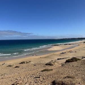 Vue panoramique d'un littoral sablonneux avec un groupe WeRoad prenant des cours de surf sur la plage et dans l'océan turquoise.