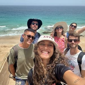 Un groupe WeRoad prend un selfie sur un point de vue surplombant une plage de sable et un océan turquoise.