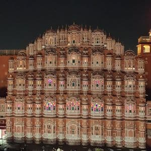 La facciata sontuosa di un palazzo in arenaria con centinaia di piccole finestre illuminate da luci colorate contro il cielo notturno.