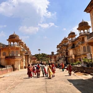 Un viaggio di gruppo WeRoad attraversa una piazza storica fiancheggiata da tradizionali e ornati edifici indiani sotto un cielo blu.