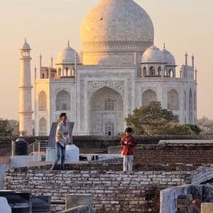 Due ragazzi su un tetto fanno volare aquiloni con il Taj Mahal sullo sfondo al tramonto.