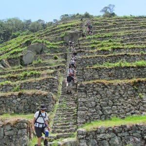 A WeRoad group trip hikes up a steep stone staircase built into grassy agricultural terraces on a mountainside.