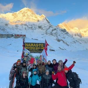 Un groupe WeRoad pose pour une photo devant le panneau du camp de base de l'Annapurna, avec des montagnes enneigées en arrière-plan.