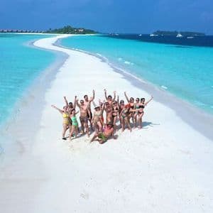 A WeRoad group trip in swimwear posing on a long white sandbar surrounded by clear turquoise water.
