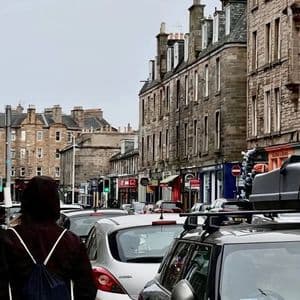 Una persona con una mochila WeRoad en una calle concurrida de la ciudad, con tráfico y edificios de piedra.
