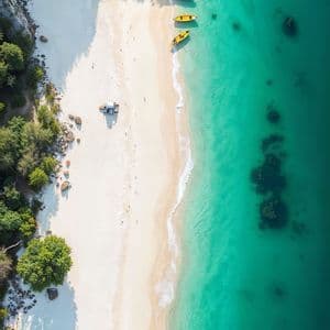 Una vista aerea dall'alto di kayak gialli allineati su una spiaggia di sabbia bianca accanto a un'acqua limpida e turchese.