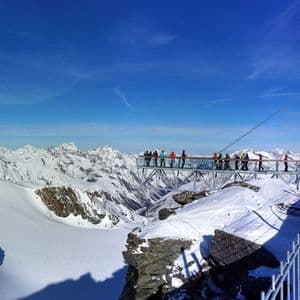 Un voyage de groupe WeRoad sur une plateforme d'observation surplombant une vaste chaîne de montagnes enneigée sous un ciel bleu clair.