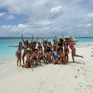 Un viaje en grupo de WeRoad posando para una foto en una playa de arena blanca con agua turquesa y un barco al fondo.