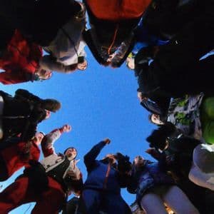 Una vista en ángulo bajo de un grupo de viaje de WeRoad reunido en círculo, mirando hacia abajo bajo un cielo azul claro.