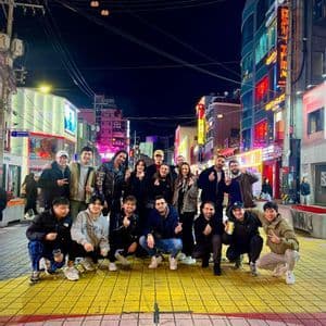 Un viaggio di gruppo WeRoad in posa per una foto su una strada di città di notte, con insegne al neon luminose sullo sfondo.