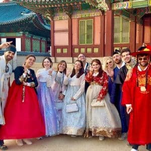 Un gruppo WeRoad sorride e posa per una foto in abiti tradizionali coreani davanti a un palazzo storico.