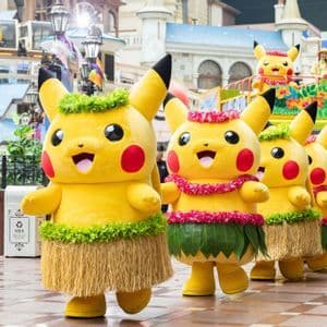 Una fila di persone in costume da Pikachu che indossano gonne di paglia e lei in stile hawaiano sfilano in parata.