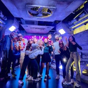 Un viaggio di gruppo WeRoad con persone che sorridono e posano con accessori da festa in una stanza a tema futuristico con luci blu.