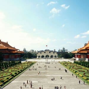 Una veduta dall'alto di una grande piazza con persone, fiancheggiata da tradizionali edifici asiatici con tetti arancioni e giardini curati.