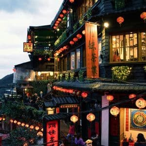 Una strada trafficata e su più livelli, affiancata da edifici tradizionali decorati con file di lanterne di carta rosse illuminate al crepuscolo.