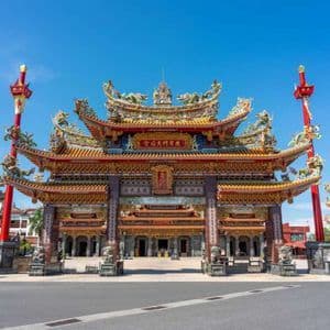 Un grande e ornato portale di un tempio dell'Asia orientale, con un tetto colorato e dettagliato, si erge al di là di una strada sotto un cielo azzurro e limpido.