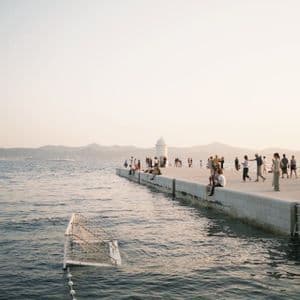 Eine WeRoad Gruppenreise auf einem langen Pier bei Sonnenuntergang, mit einem Wasserballtor, das im Meer schwimmt.