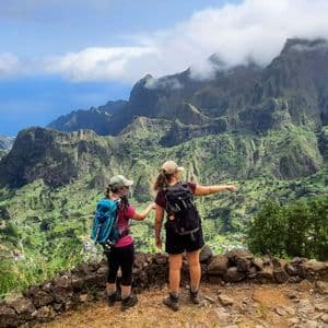 Zwei Frauen auf einer WeRoad Gruppenreise mit Rucksäcken zeigen von einem Aussichtspunkt auf ein üppiges, grünes Bergtal.