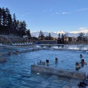 Eine WeRoad Gruppenreise entspannt in einem Outdoor-Thermalbad mit Blick auf schneebedeckte Berge.