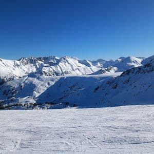 Une vaste chaîne de montagnes enneigée s'étend sous un ciel bleu profond et dégagé par une journée ensoleillée.