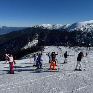 Un groupe WeRoad posant à ski sur une pente de montagne enneigée, sous un ciel bleu clair, avec des montagnes boisées en arrière-plan.