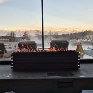 Un voyage de groupe WeRoad se détendant dans une piscine extérieure fumante avec un grand brasero devant des montagnes enneigées.