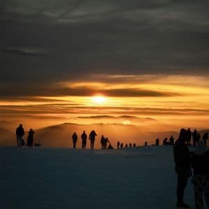 Sagome di un viaggio di gruppo WeRoad su una cresta di montagna innevata che osservano un'alba dorata su vette lontane.