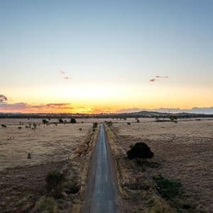 Vue aérienne d'une route droite s'étendant à travers une vaste savane sèche vers le soleil couchant à l'horizon.