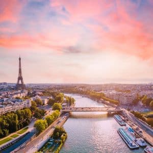 Una vista aerea dello skyline di Parigi con la Torre Eiffel e il fiume Senna sotto un tramonto drammatico rosa e arancione.