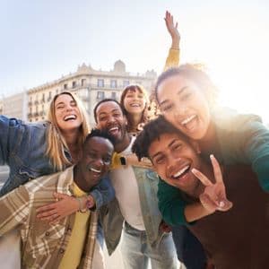 Un viaggio di gruppo WeRoad di amici che ridono e sorridono mentre si scattano un selfie su una strada di città soleggiata.