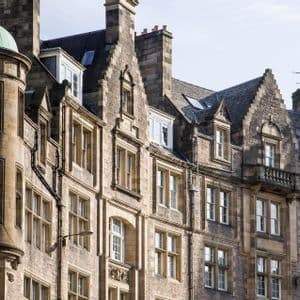 Una vista ravvicinata dei piani superiori di edifici tradizionali in pietra, con una cupola di rame verde su una torretta.
